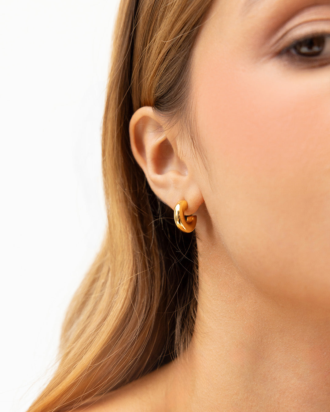 Medio rostro de mujer con enfoque en su oreja las candongas Classic en baño de oro